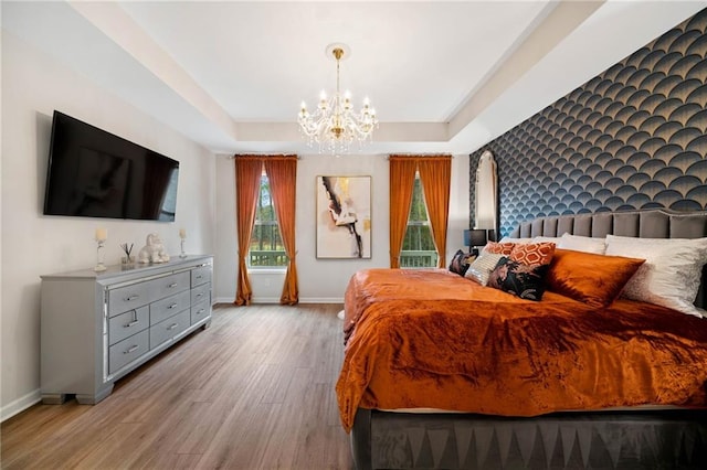 bedroom featuring a tray ceiling, a notable chandelier, wood finished floors, and baseboards