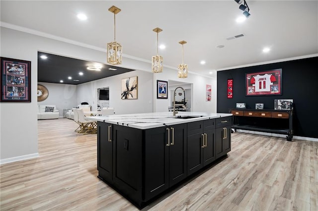 kitchen featuring visible vents, a sink, light wood finished floors, dark cabinets, and light countertops