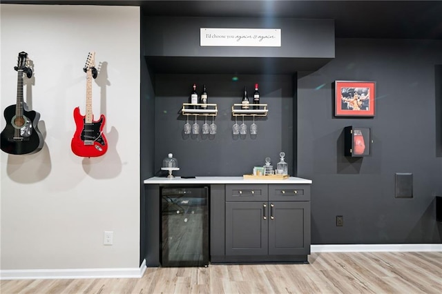 bar with light wood-style flooring, baseboards, beverage cooler, and a dry bar