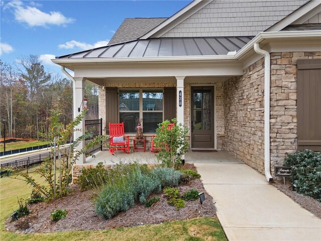 entrance to property with fence, a standing seam roof, covered porch, stone siding, and metal roof