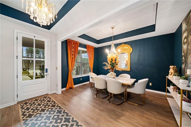 dining area with wood finished floors, baseboards, a raised ceiling, and a chandelier