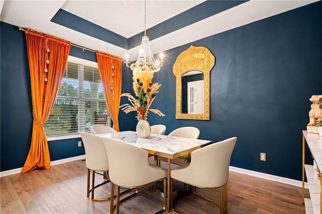 dining space with a tray ceiling, wood finished floors, and baseboards