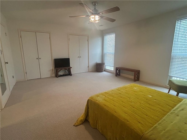 bedroom featuring multiple windows, light carpet, two closets, and a ceiling fan