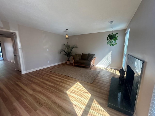 unfurnished living room featuring wood finished floors, baseboards, visible vents, a fireplace with raised hearth, and a textured ceiling