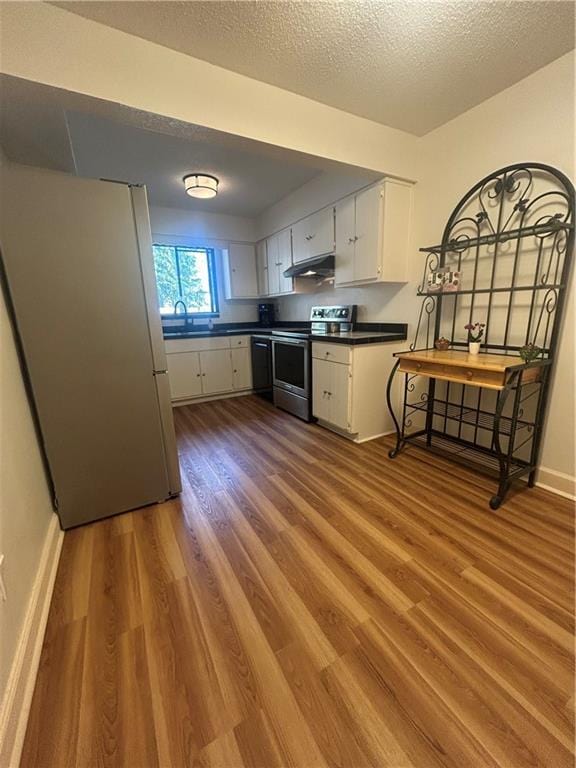 kitchen featuring electric range, under cabinet range hood, dark countertops, wood finished floors, and freestanding refrigerator