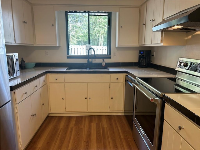 kitchen with dark wood-type flooring, electric stove, under cabinet range hood, a sink, and tile counters