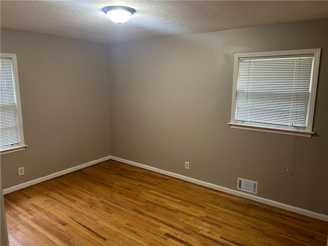 empty room with a textured ceiling, wood finished floors, visible vents, and baseboards