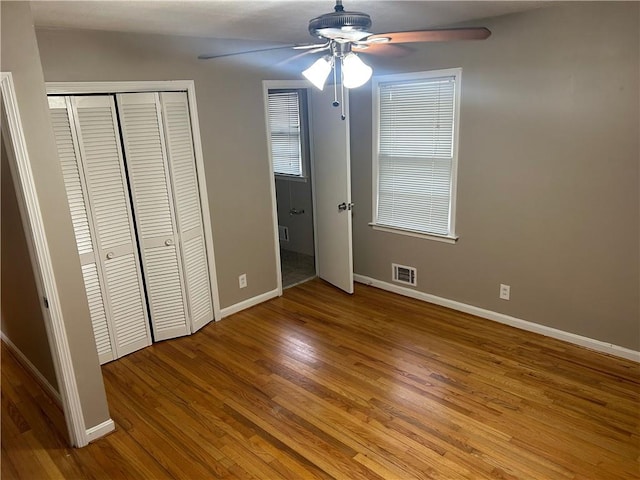 unfurnished bedroom with a ceiling fan, visible vents, wood finished floors, baseboards, and a closet