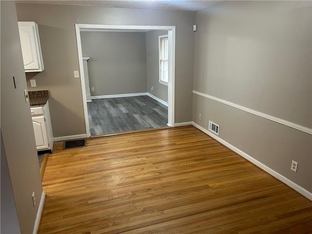 unfurnished dining area with wood finished floors, visible vents, and baseboards