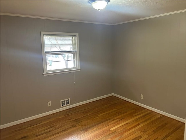 spare room with visible vents, ornamental molding, baseboards, and wood finished floors