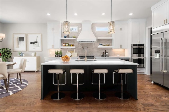 kitchen featuring pendant lighting, custom exhaust hood, an island with sink, and appliances with stainless steel finishes