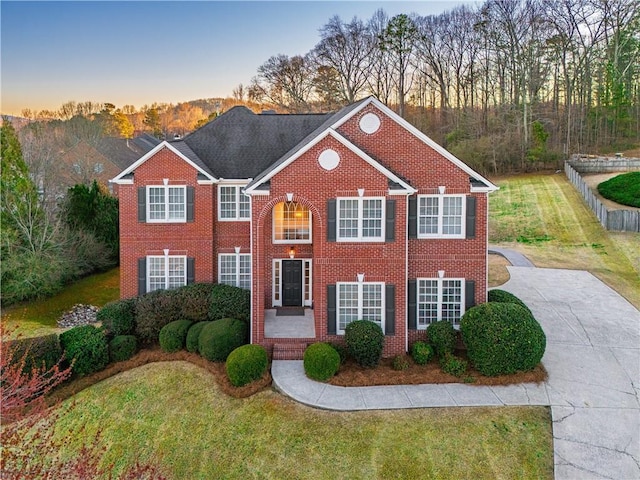 view of front of house with a front lawn, concrete driveway, fence, and brick siding