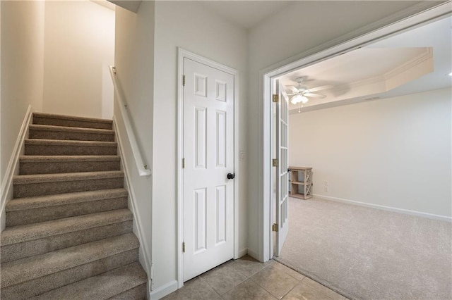 stairs featuring ceiling fan, baseboards, carpet, a tray ceiling, and tile patterned floors