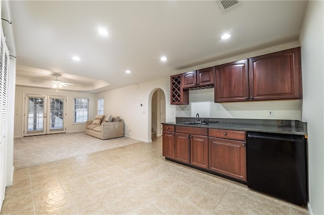 kitchen featuring visible vents, a tray ceiling, dark countertops, arched walkways, and dishwasher