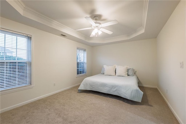 carpeted bedroom featuring a tray ceiling, a ceiling fan, baseboards, and ornamental molding