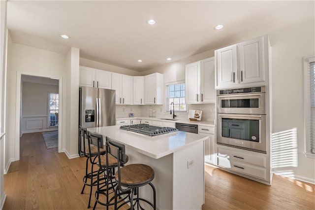 kitchen featuring light wood-type flooring, a sink, a kitchen breakfast bar, stainless steel appliances, and white cabinets