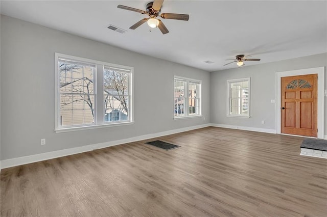 unfurnished living room featuring a ceiling fan, visible vents, baseboards, and wood finished floors