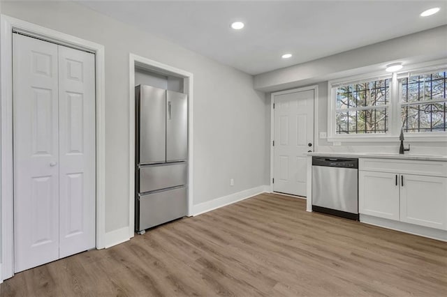 kitchen with light countertops, light wood-style flooring, appliances with stainless steel finishes, white cabinets, and a sink