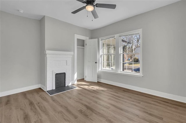 unfurnished living room featuring ceiling fan, a fireplace, baseboards, and wood finished floors