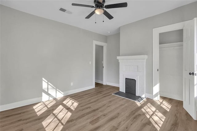 unfurnished living room with a brick fireplace, baseboards, visible vents, and wood finished floors