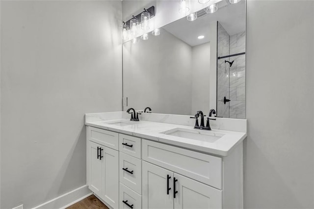 full bath with double vanity, baseboards, a sink, and tiled shower