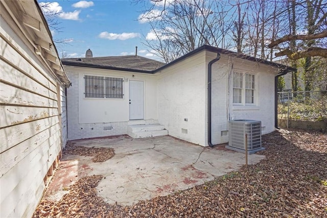 view of exterior entry with brick siding, central air condition unit, crawl space, a patio area, and fence