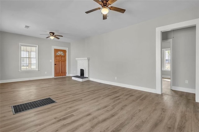 unfurnished living room featuring a brick fireplace, visible vents, and a healthy amount of sunlight