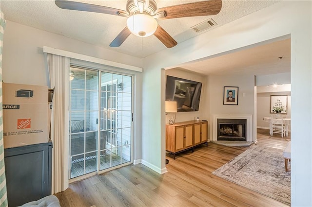 215 Cobblestone Trl, Avondale Estates, GA 30002 - living room featuring light wood-style flooring, a ceiling fan, a fireplace with raised hearth, baseboards, and a textured ceiling