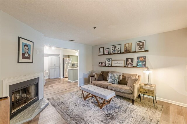 215 Cobblestone Trl, Avondale Estates, GA 30002 - living room featuring light wood-type flooring, baseboards, a fireplace with raised hearth, and a textured ceiling