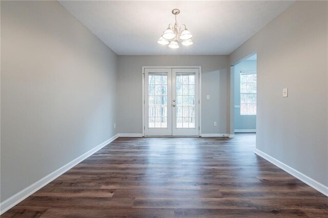 empty room featuring a notable chandelier, dark hardwood / wood-style flooring, and french doors