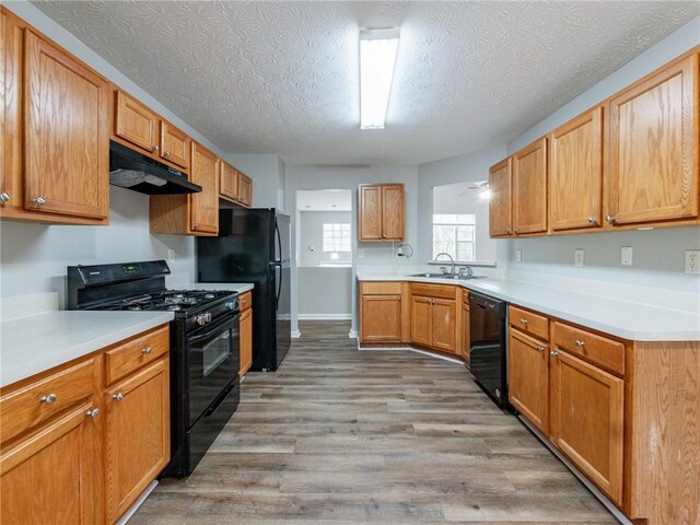 kitchen with light hardwood / wood-style flooring, black appliances, a textured ceiling, and sink