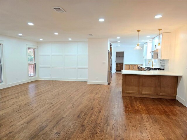 kitchen featuring hardwood / wood-style floors, sink, hanging light fixtures, decorative backsplash, and kitchen peninsula