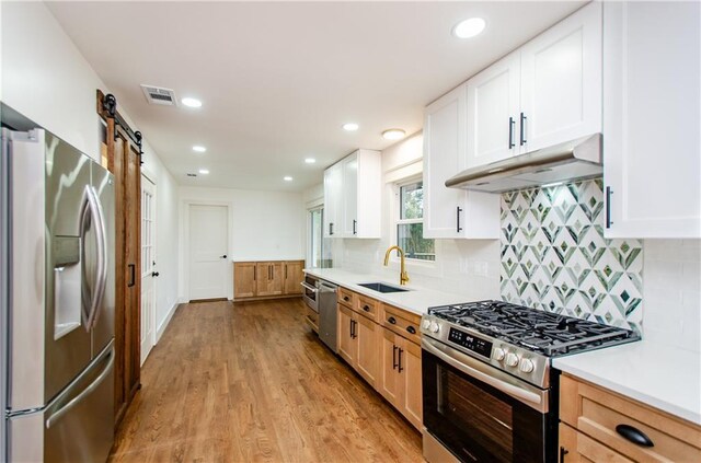 kitchen featuring tasteful backsplash, stainless steel appliances, sink, a barn door, and white cabinets