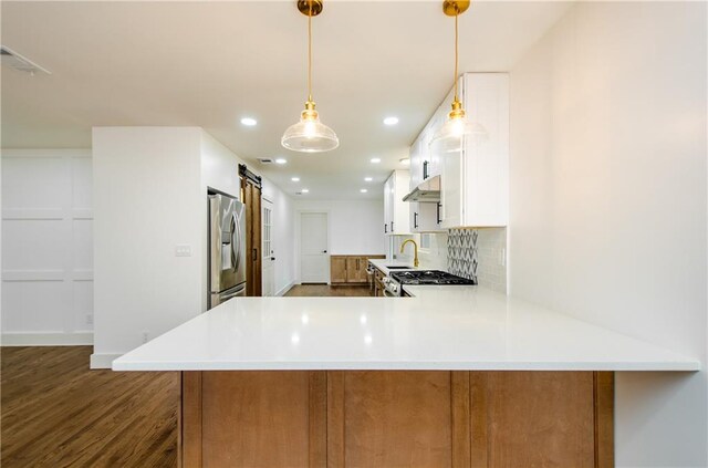 kitchen with kitchen peninsula, pendant lighting, a barn door, stainless steel fridge with ice dispenser, and white cabinetry