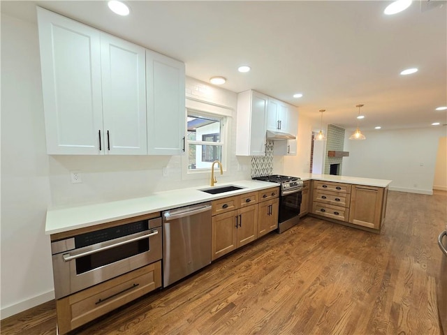 kitchen with kitchen peninsula, stainless steel appliances, sink, white cabinetry, and hanging light fixtures