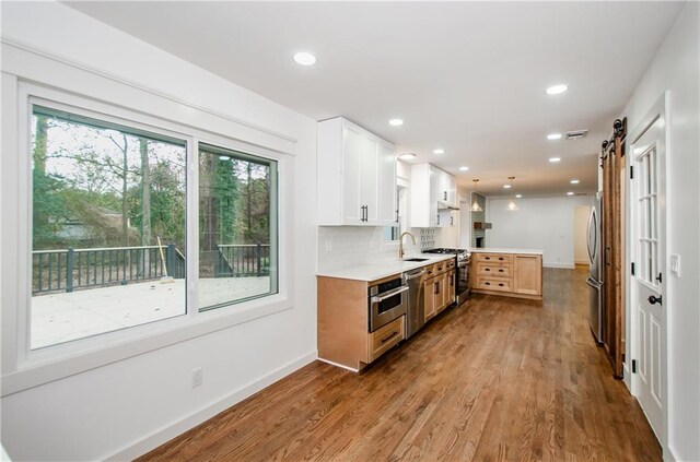 kitchen featuring sink, a barn door, backsplash, white cabinets, and appliances with stainless steel finishes