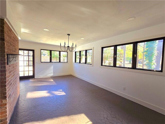 unfurnished room featuring a notable chandelier, a wealth of natural light, and a brick fireplace