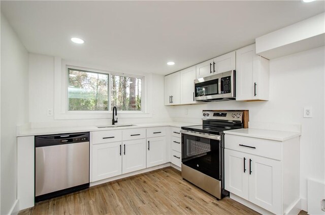 kitchen with white cabinets, appliances with stainless steel finishes, light hardwood / wood-style flooring, and sink