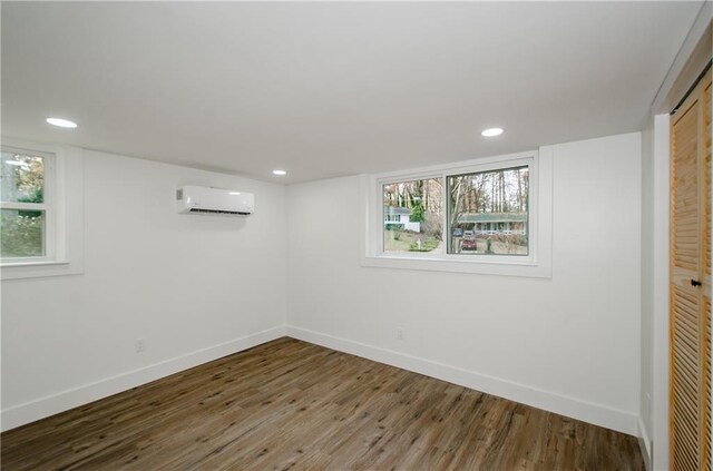 basement featuring wood-type flooring, an AC wall unit, and a healthy amount of sunlight