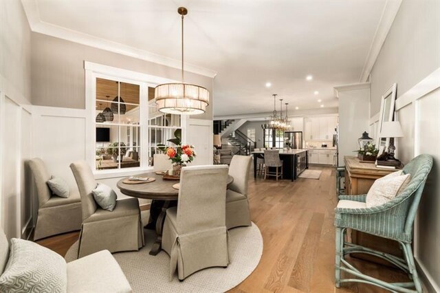 dining area featuring a wainscoted wall, light wood-type flooring, an inviting chandelier, stairs, and ornamental molding