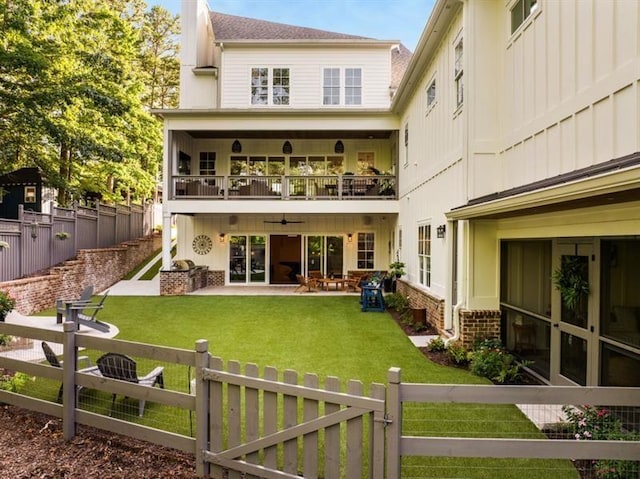 rear view of house featuring a lawn, ceiling fan, a fenced backyard, and a balcony