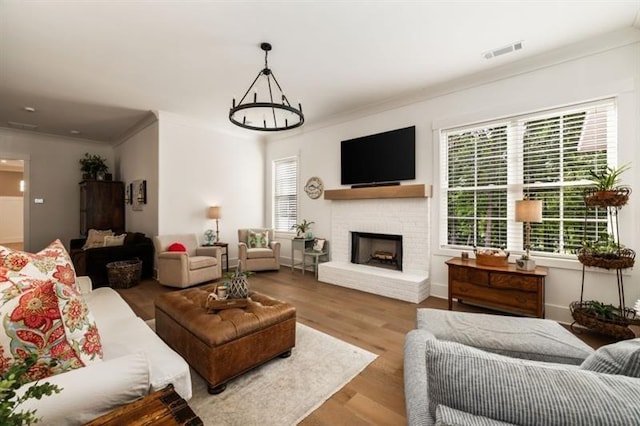 living room with baseboards, visible vents, wood finished floors, crown molding, and a fireplace