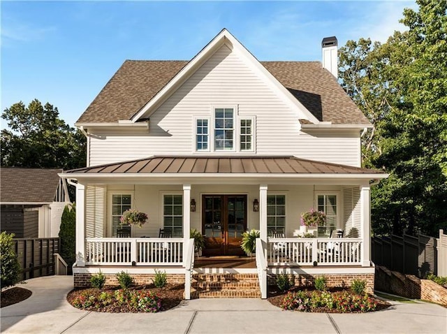 country-style home featuring a chimney, a standing seam roof, french doors, covered porch, and metal roof