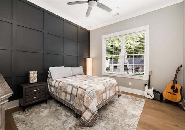 bedroom with light wood finished floors, baseboards, visible vents, a decorative wall, and ornamental molding