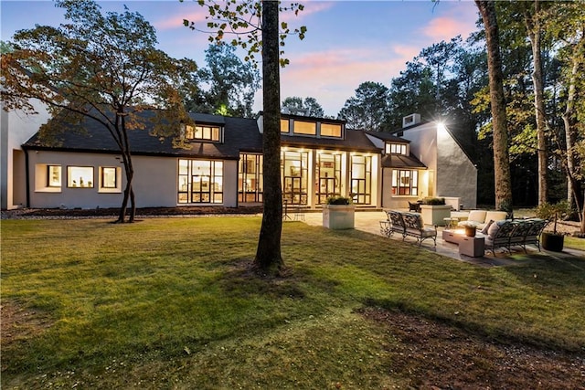 back house at dusk with an outdoor living space, a patio, and a yard