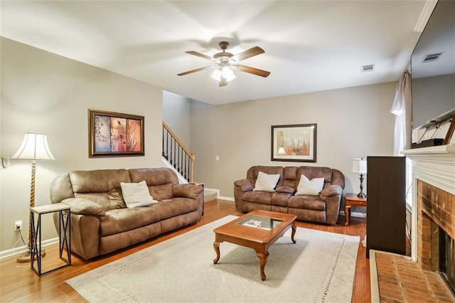 living room featuring ceiling fan, light hardwood / wood-style floors, and a brick fireplace