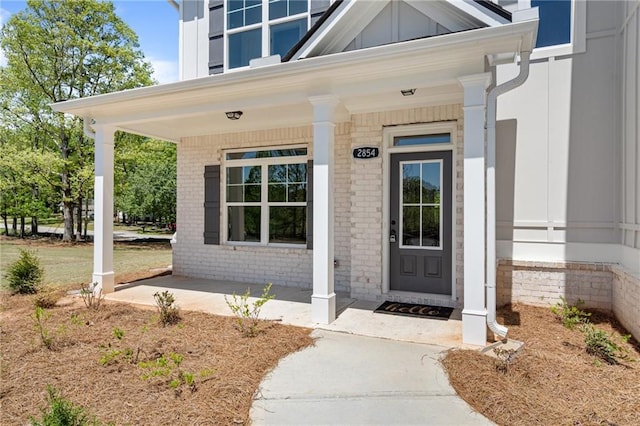 entrance to property featuring covered porch, board and batten siding, and brick siding