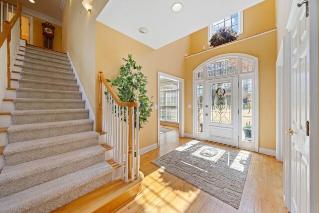 foyer entrance with hardwood / wood-style flooring, ornamental molding, a high ceiling, and ceiling fan with notable chandelier