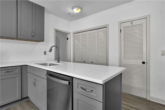 kitchen with wood finished floors, a peninsula, a sink, gray cabinets, and stainless steel dishwasher