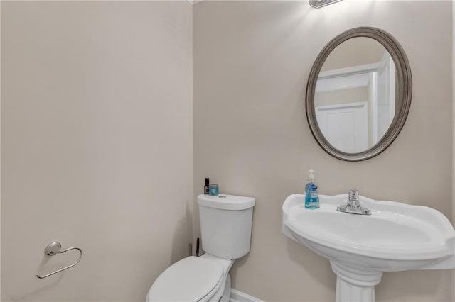 half bath with baseboards, a sink, and toilet